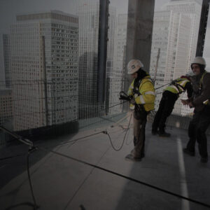 Operative wearing hi-vis, hard hat and harness securing a safe anchorage point