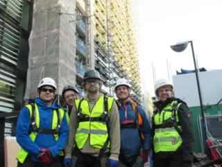 5 operatives wearing working at height safety harness standing in front of tall building