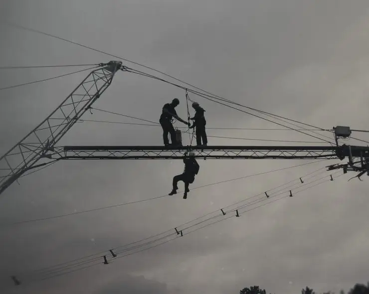 Construction workers in height safety gear. One worker in fall arrest position, while other two workers carry out rescue procedure.